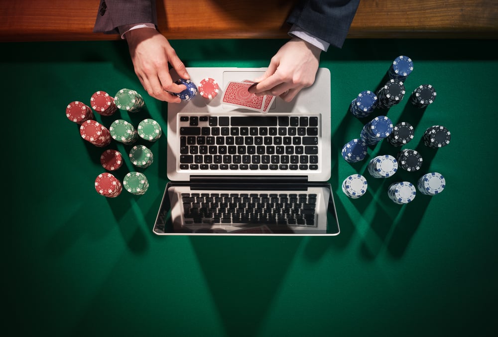 man playing online poker on laptop with poker chips scattered around